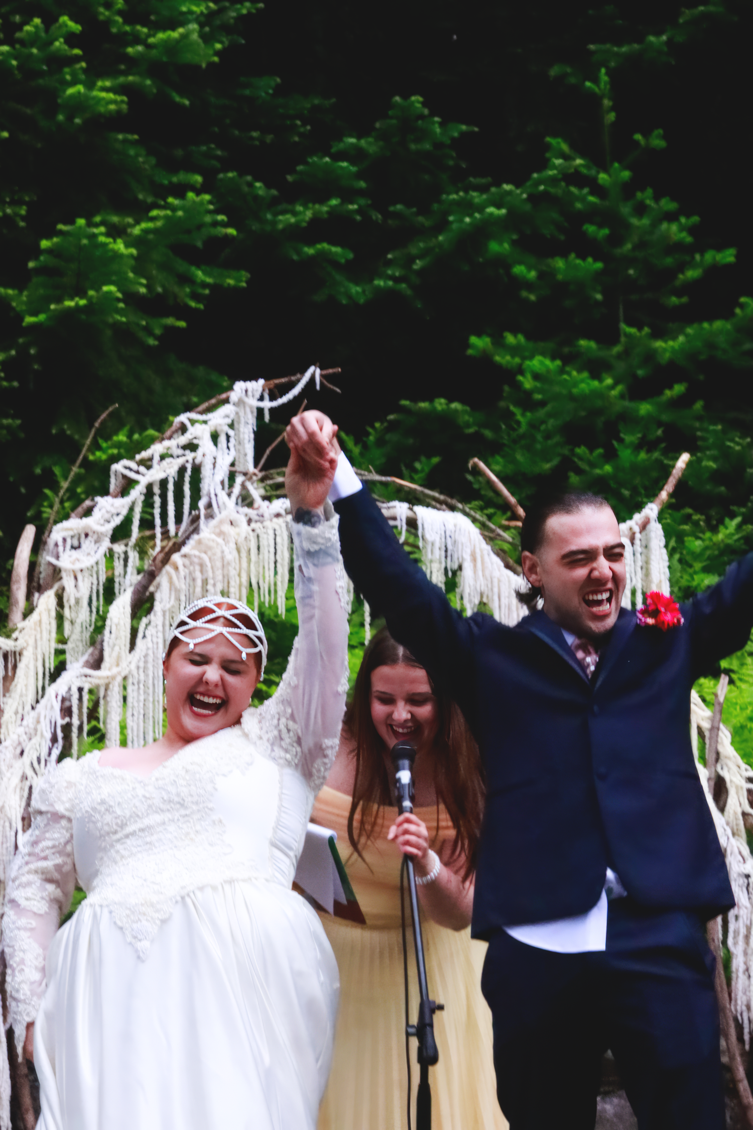 Newlyweds celebrate joyfully under a decorative white arch with greenery backdrop at their wedding ceremony.