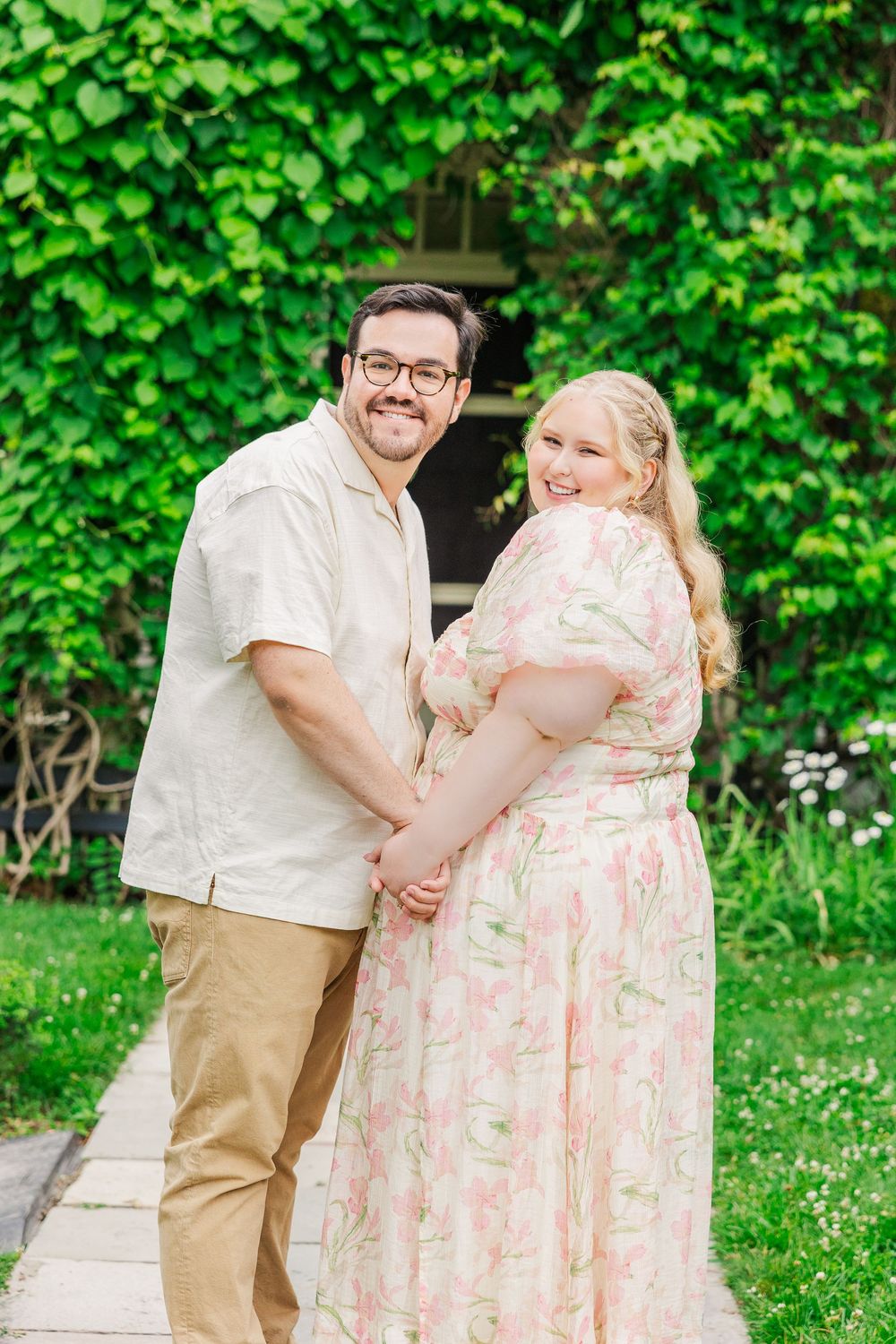 A couple shares romantic moments in a lush green garden setting wearing coordinated spring outfits.