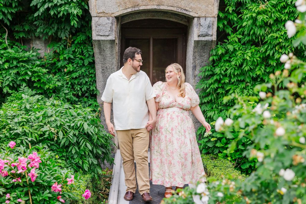 A couple stands together in a romantic garden setting framed by a stone archway and lush greenery.
