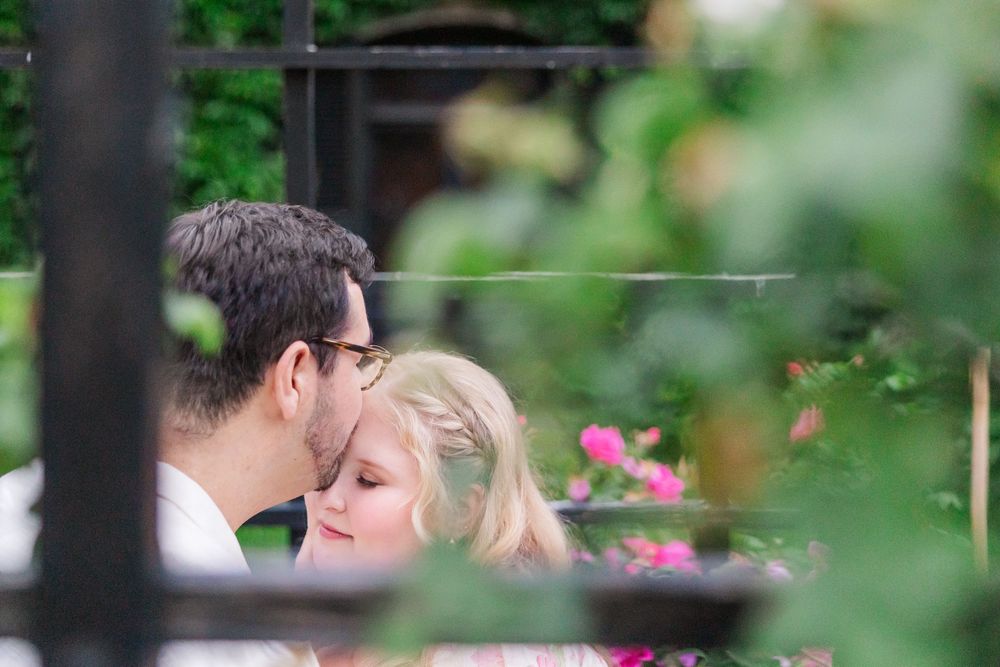 Pink roses frame an intimate moment between a couple in a peaceful garden setting.