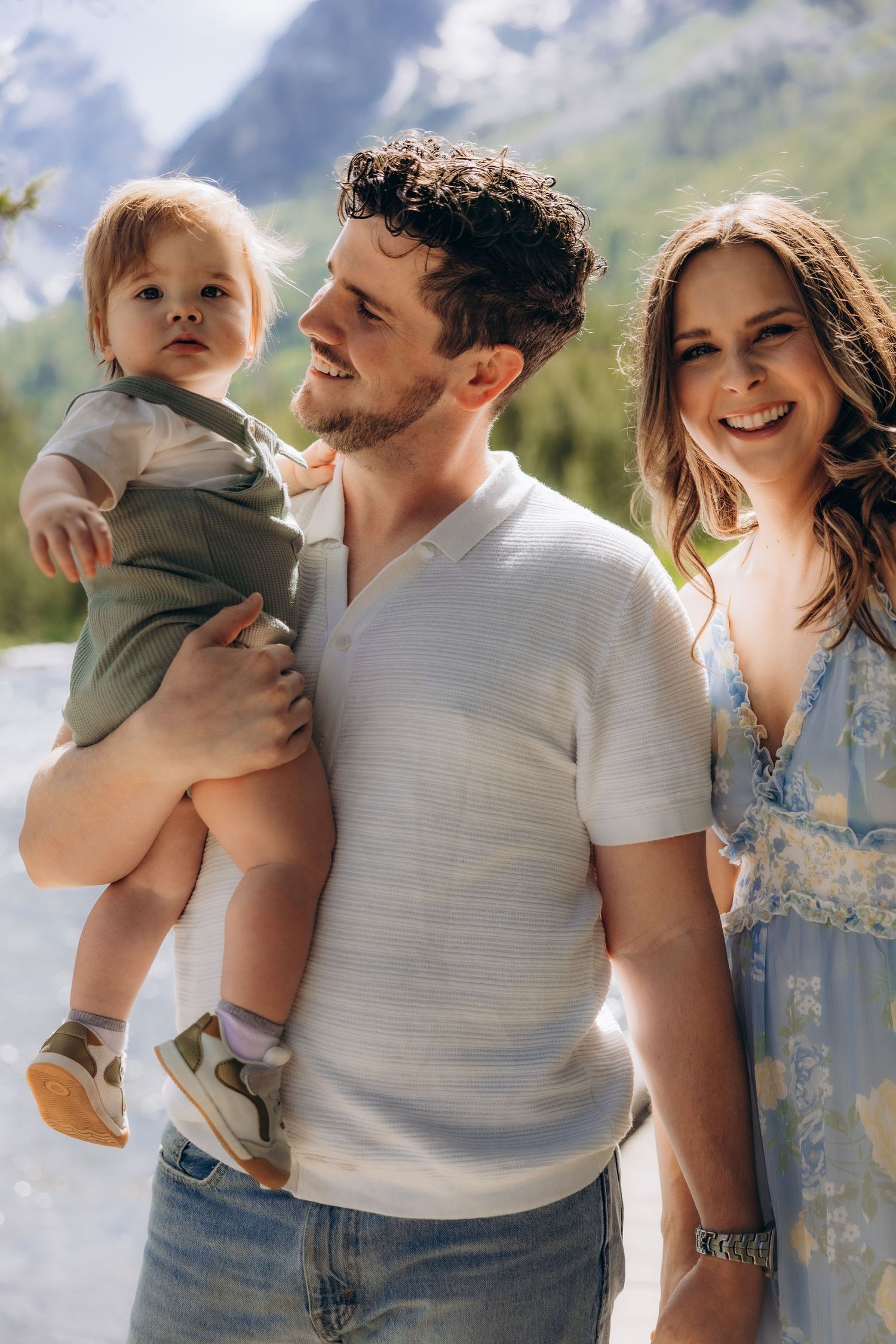 A young family embraces while wearing casual attire against a mountainous landscape.