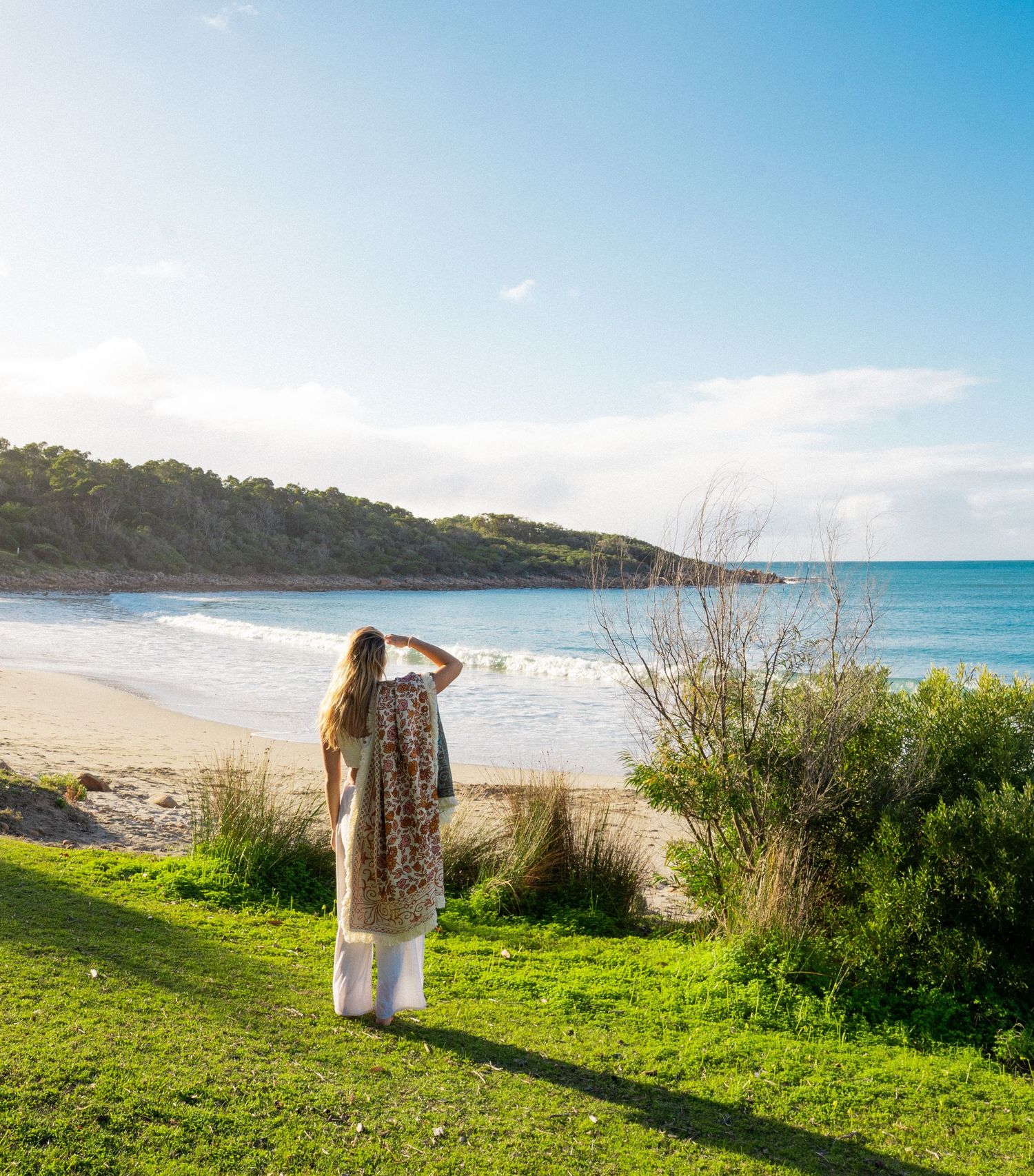 Person in flowing dress overlooking scenic coastal beach view.