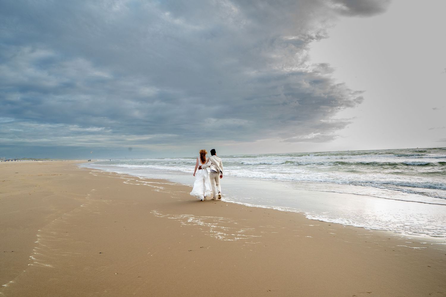 Bruidspaar maakt een strandwandeling met dreigende stormwolken