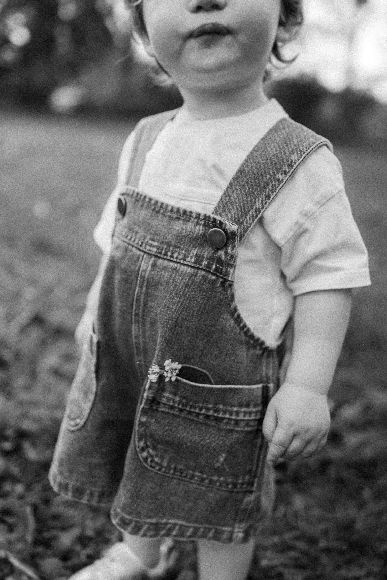 Close-up black and white photo series of a child wearing denim overalls and a white t-shirt in an outdoor setting.