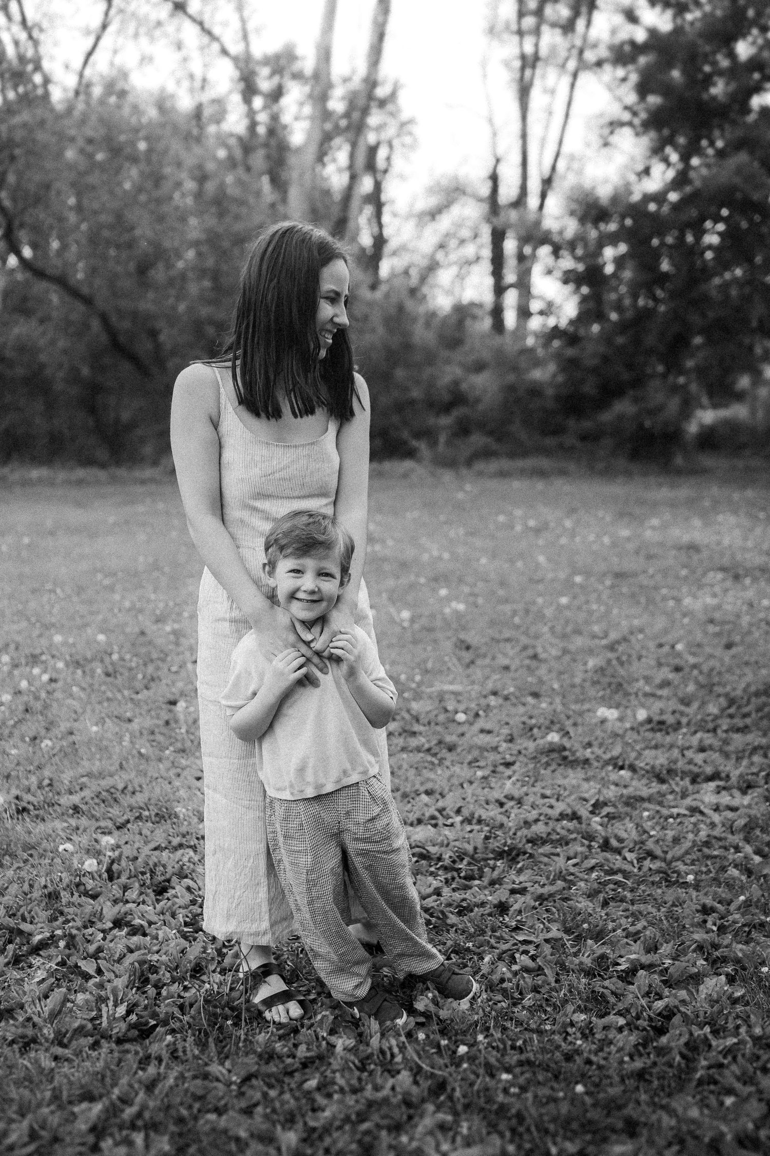 Black and white photo of playful interaction between parent and child in a field surrounded by fallen leaves.