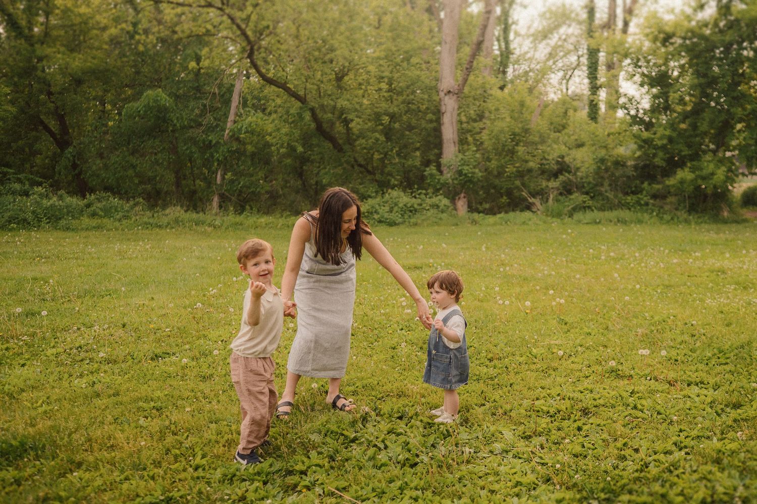 Three people play together in a sunny green field surrounded by trees on a warm afternoon.