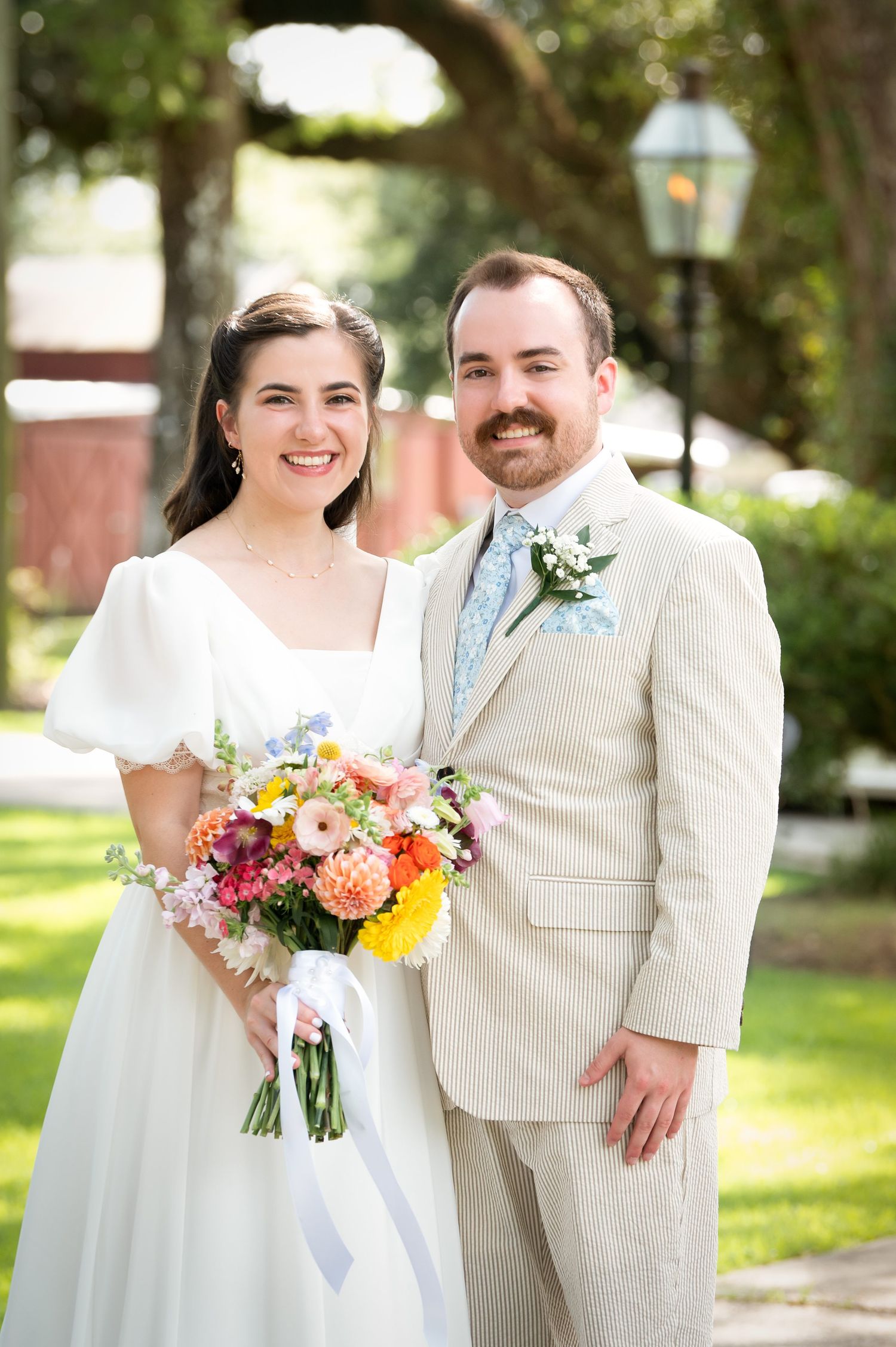 Wedding couple holds vibrant spring bouquet while posing in an outdoor garden setting.