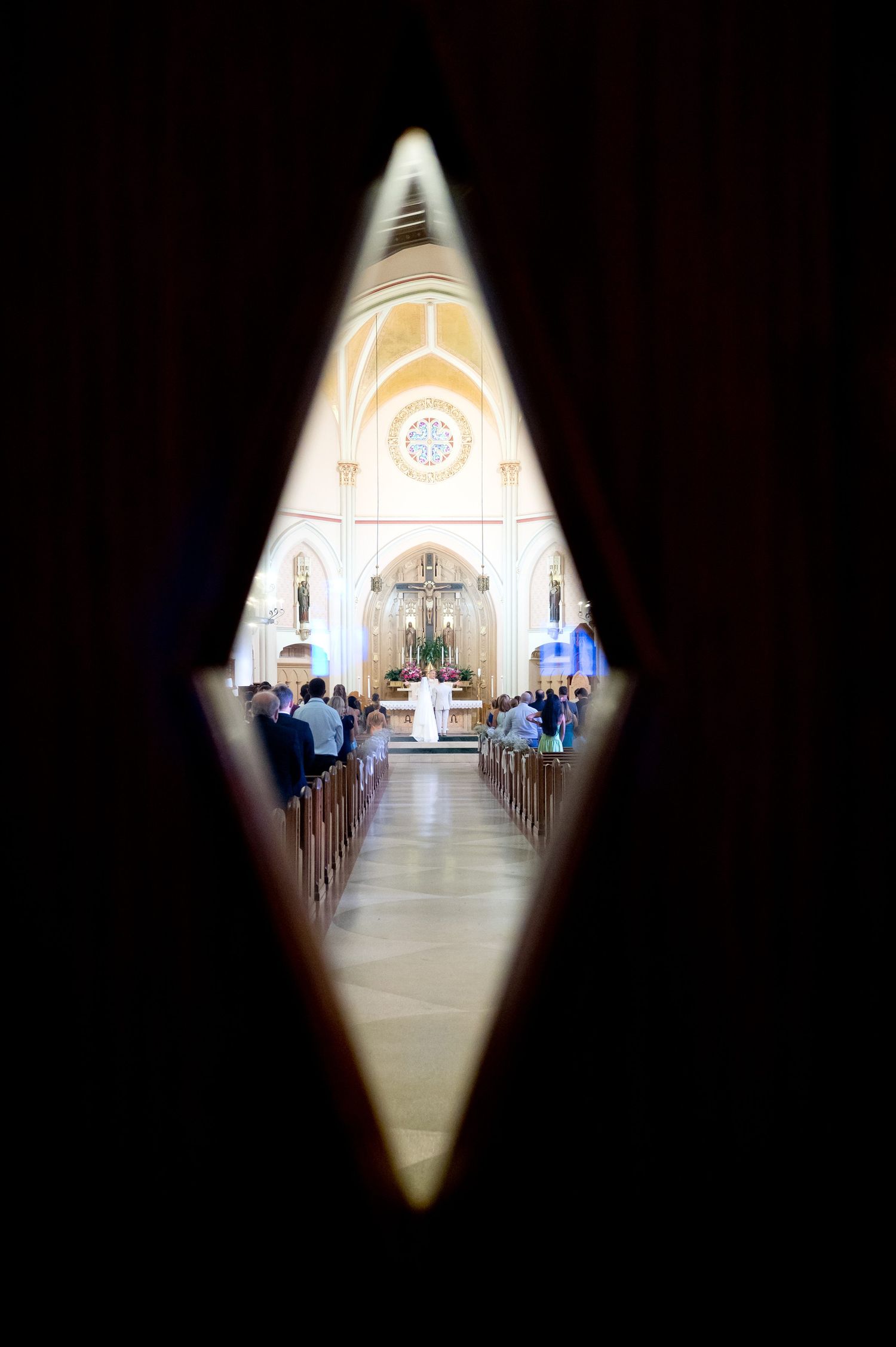 View through a diamond-shaped doorway of a traditional church interior during a wedding ceremony.