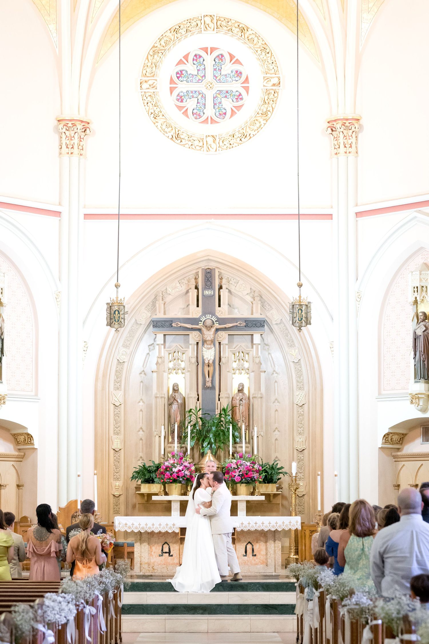 Wedding ceremony in a beautiful white church with ornate altar and floral decorations.