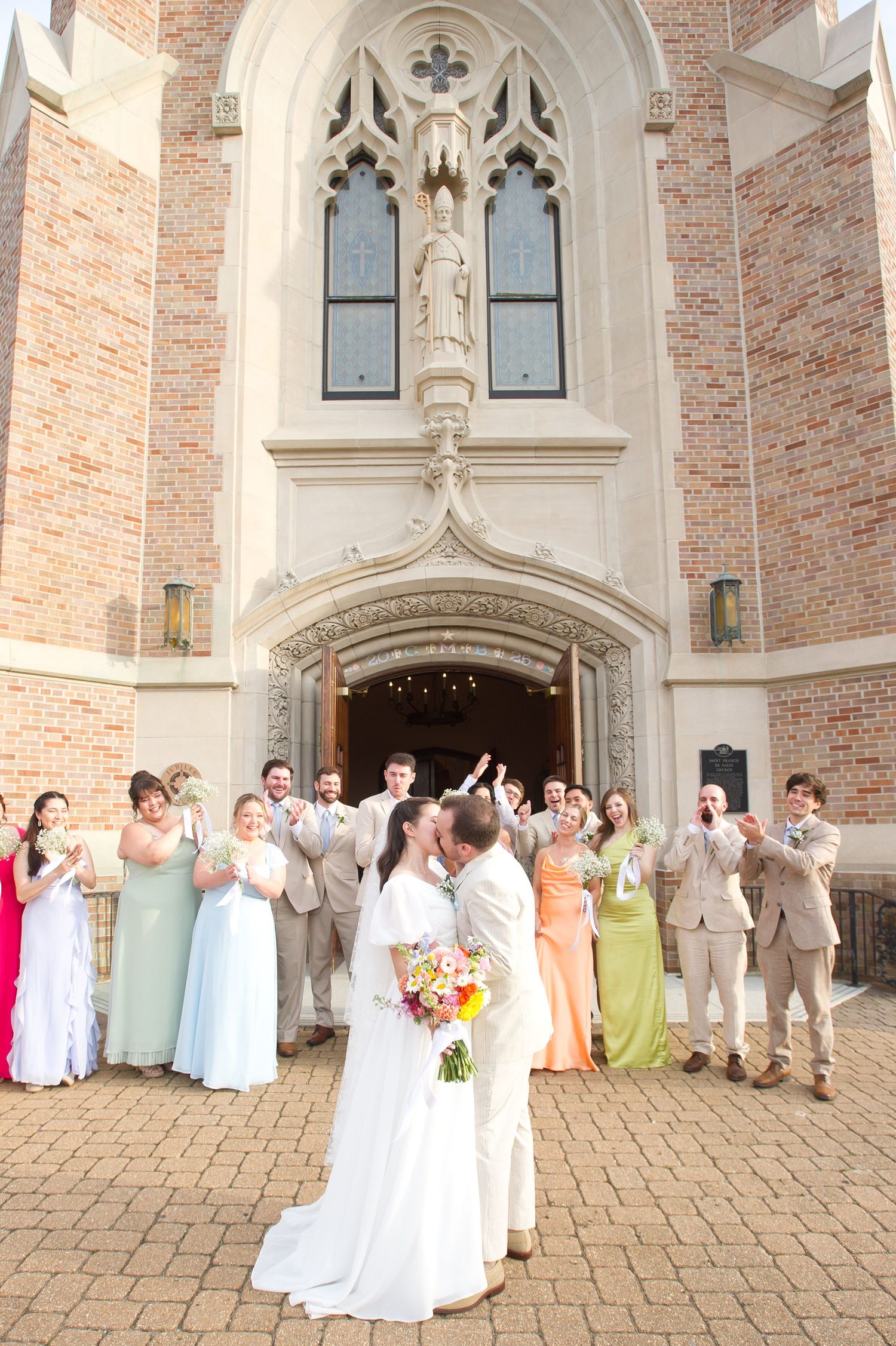 Wedding party celebrating outside a Gothic church entrance with brick and stone architecture.
