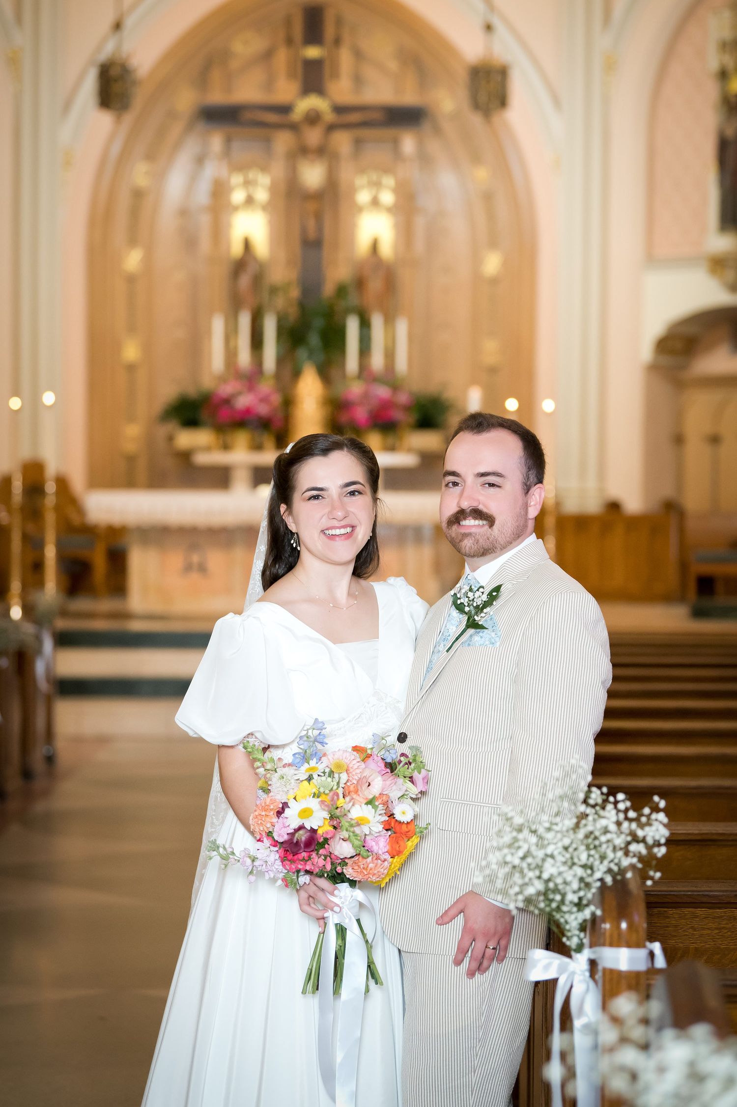 Newlyweds pose in church sanctuary with colorful bridal bouquet.