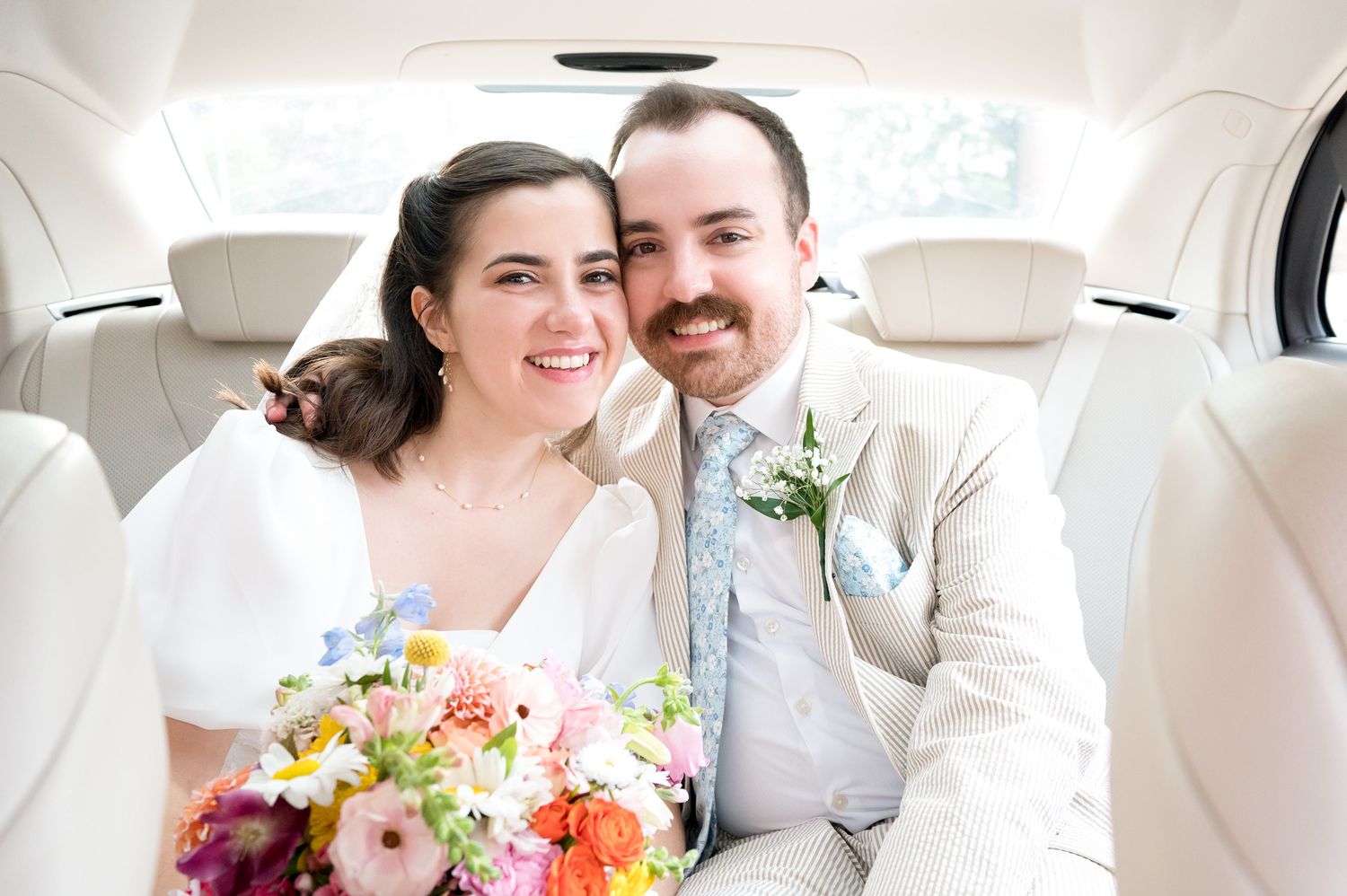 Newlyweds sharing a moment in the backseat of a car with floral bouquet.