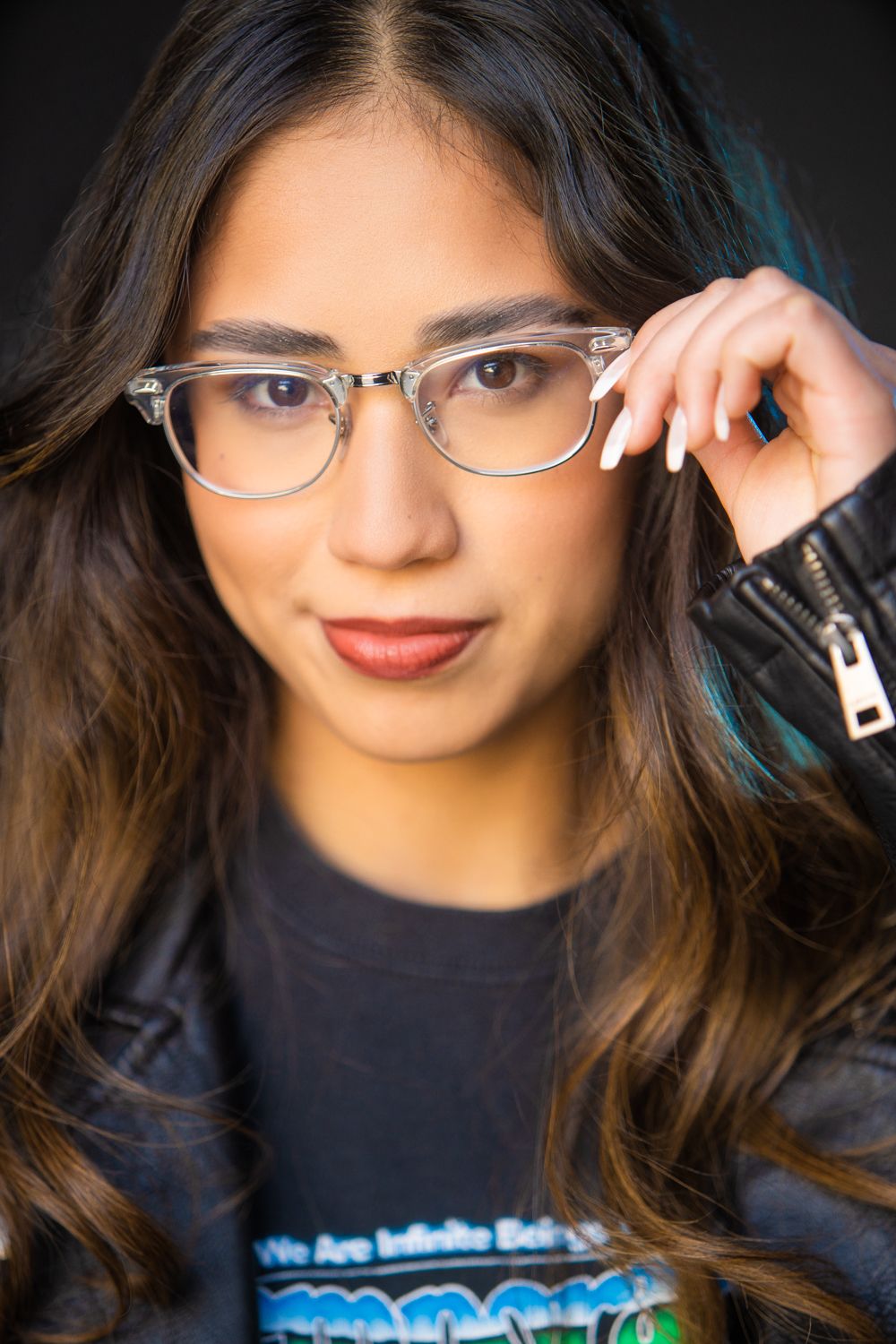 A portrait with long dark hair, glasses, and a navy blue top featuring digital lights against a black background.