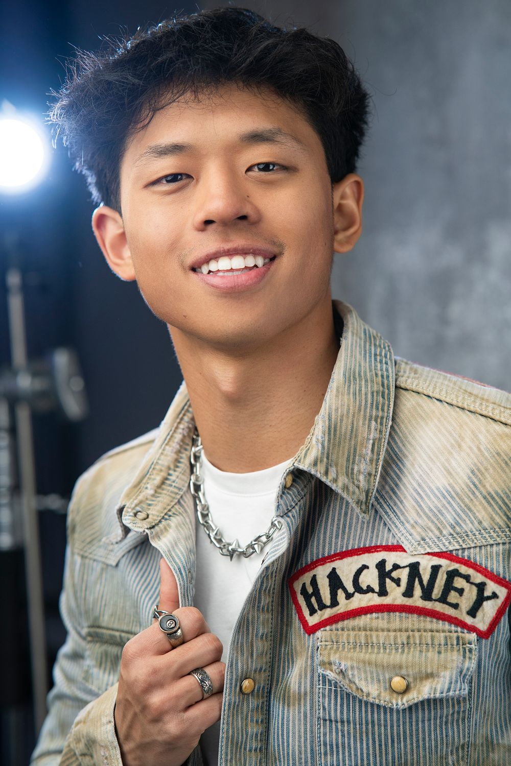Person wearing a beige jacket with Hackney patch smiles and poses in multiple shots against dark background.