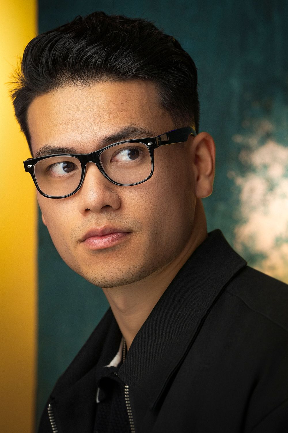 Professional portrait photo series showing different angles of someone wearing glasses and a black jacket against dark and yellow backdrop.