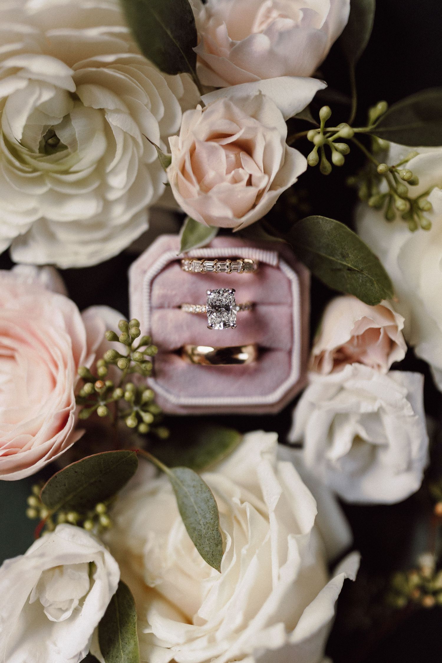 Wedding rings nestled among blush and white roses with greenery.