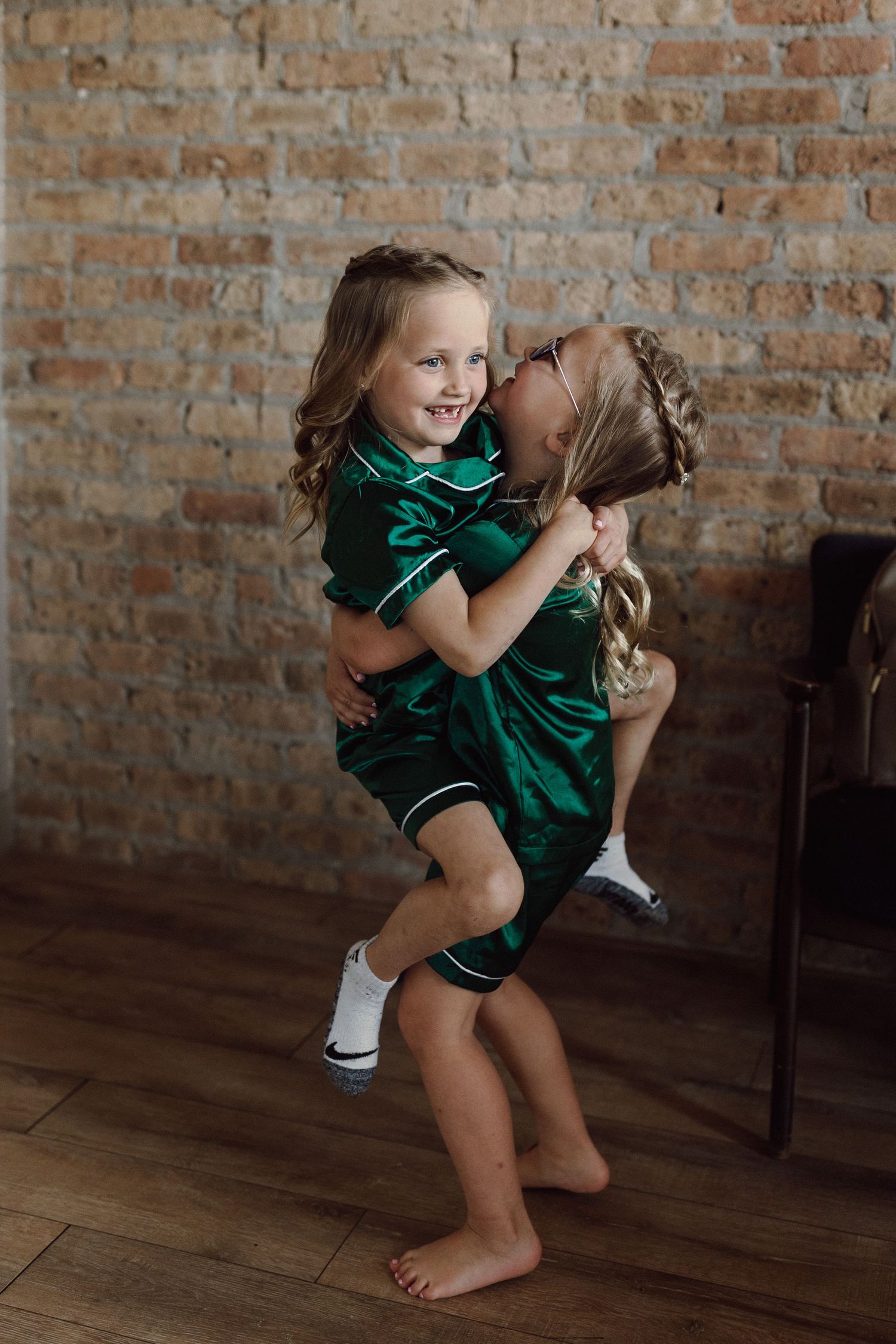 A playful child in emerald green pajamas dancing against a brick wall background.