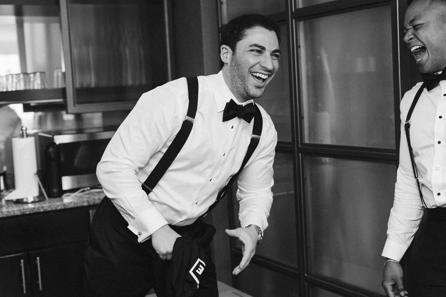 Black and white photo of groom laughing while getting ready on wedding day.