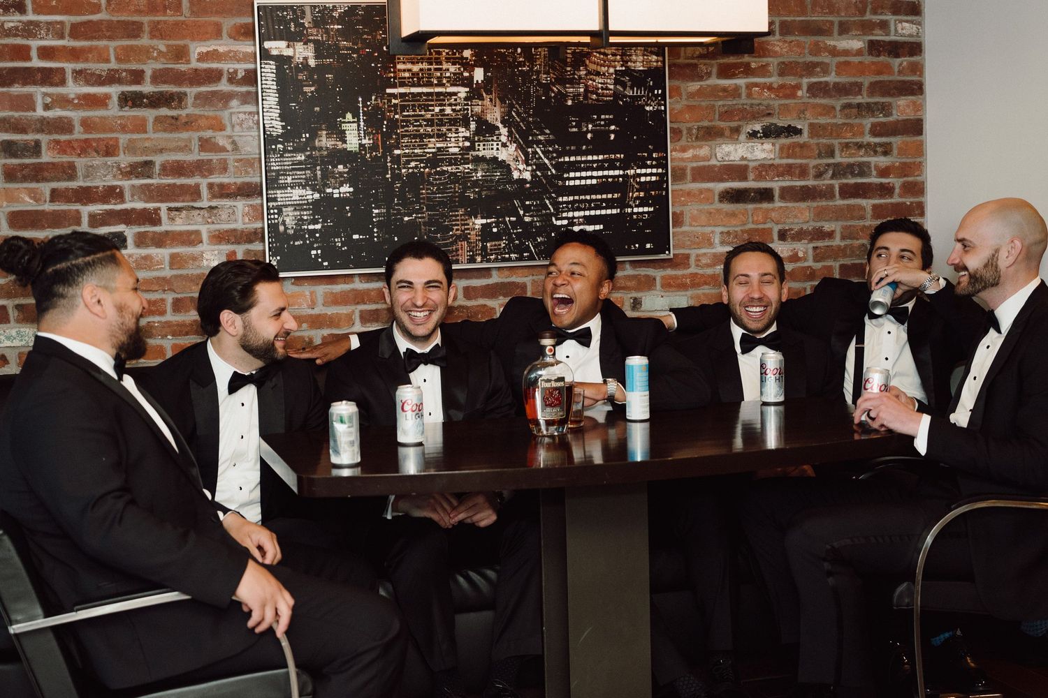 Groomsmen in tuxedos gather around table for drinks at wedding reception.