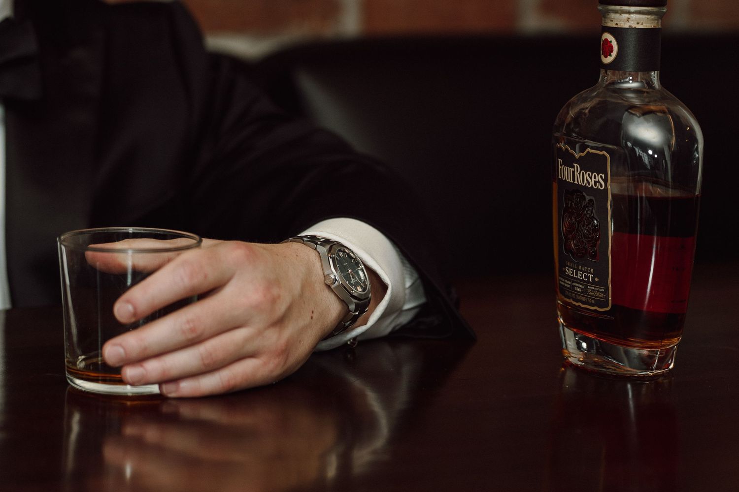 Close-up of hand holding whiskey glass next to bottle on wooden table.
