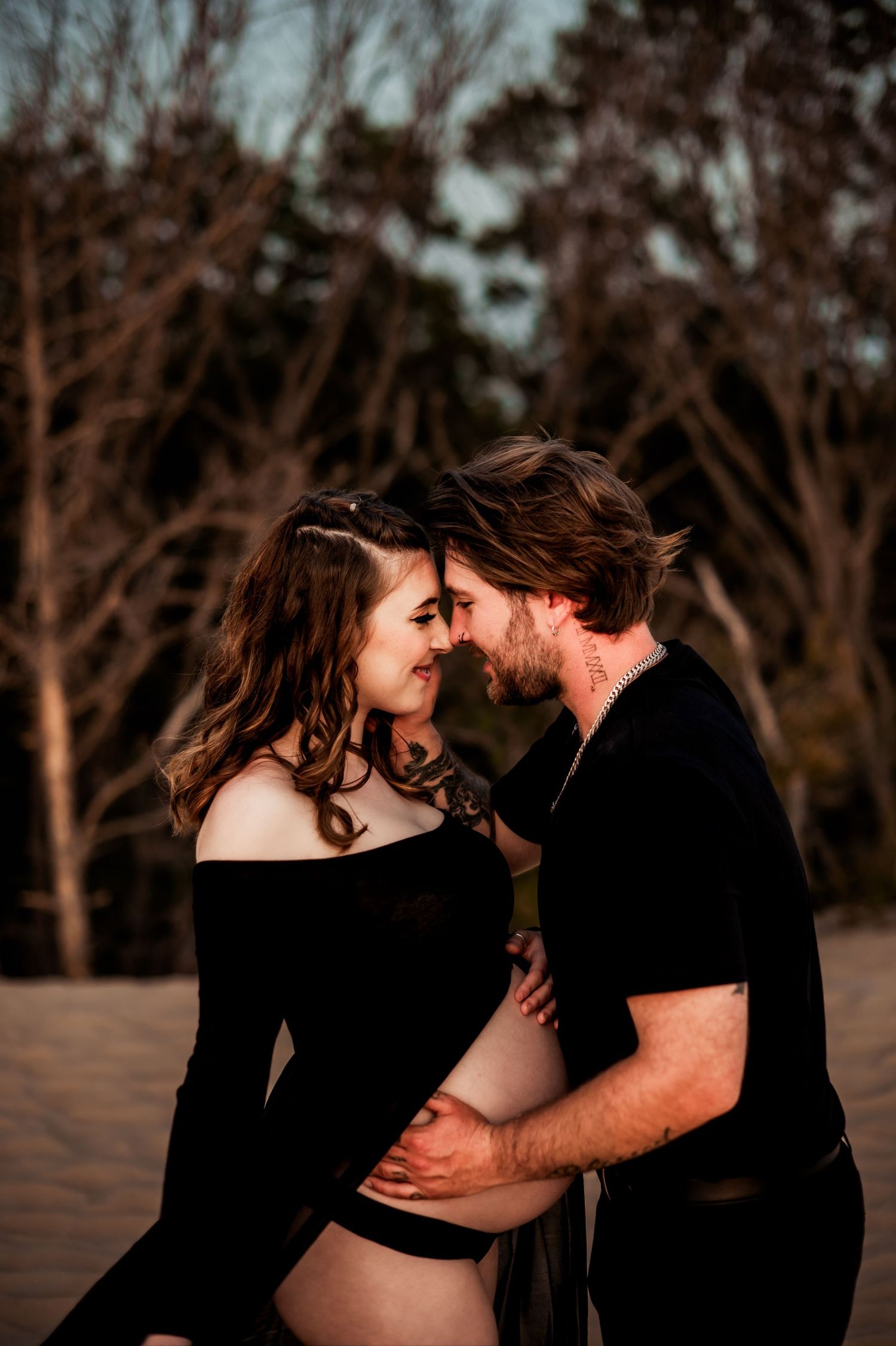 An intimate maternity photo captures a romantic moment between expectant parents against a dusky forest backdrop atop Silver Lake Dunes