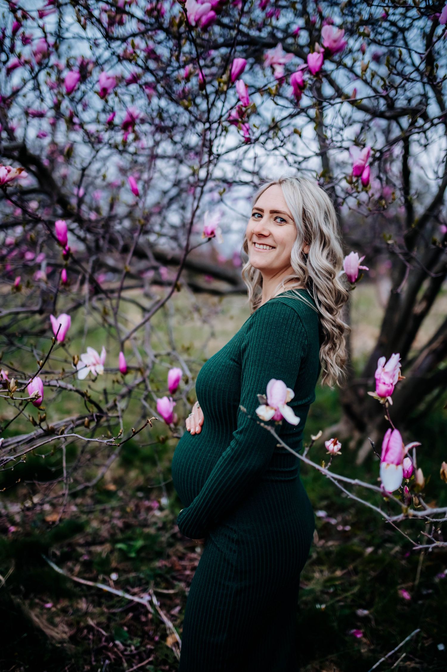 Person wearing a green sweater poses near blooming pink magnolia flowers on a spring day at Highlands Park