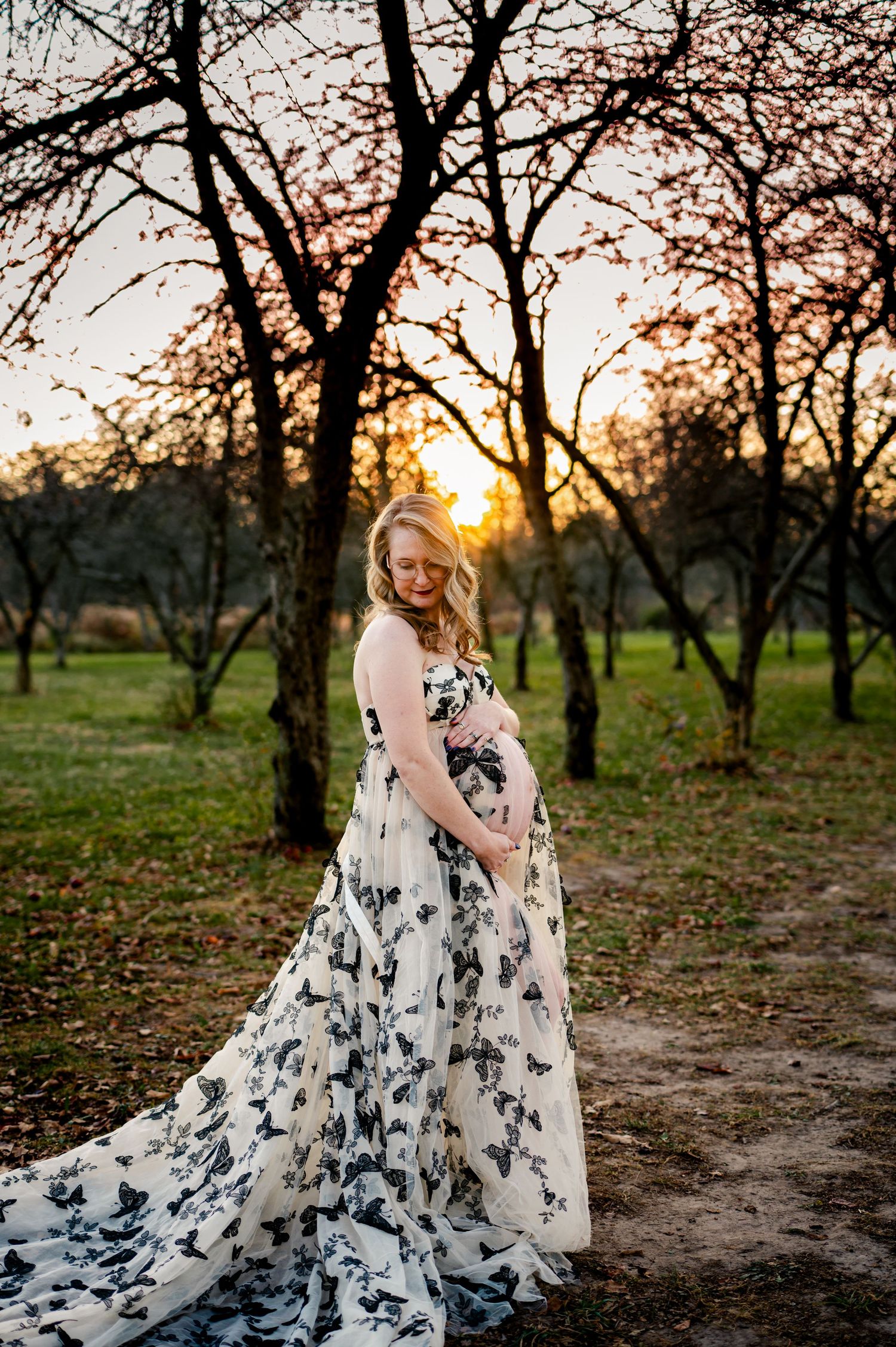 Elegant flowing butterfly print gown photographed in a rustic orchard at sunset with dreamy lighting.