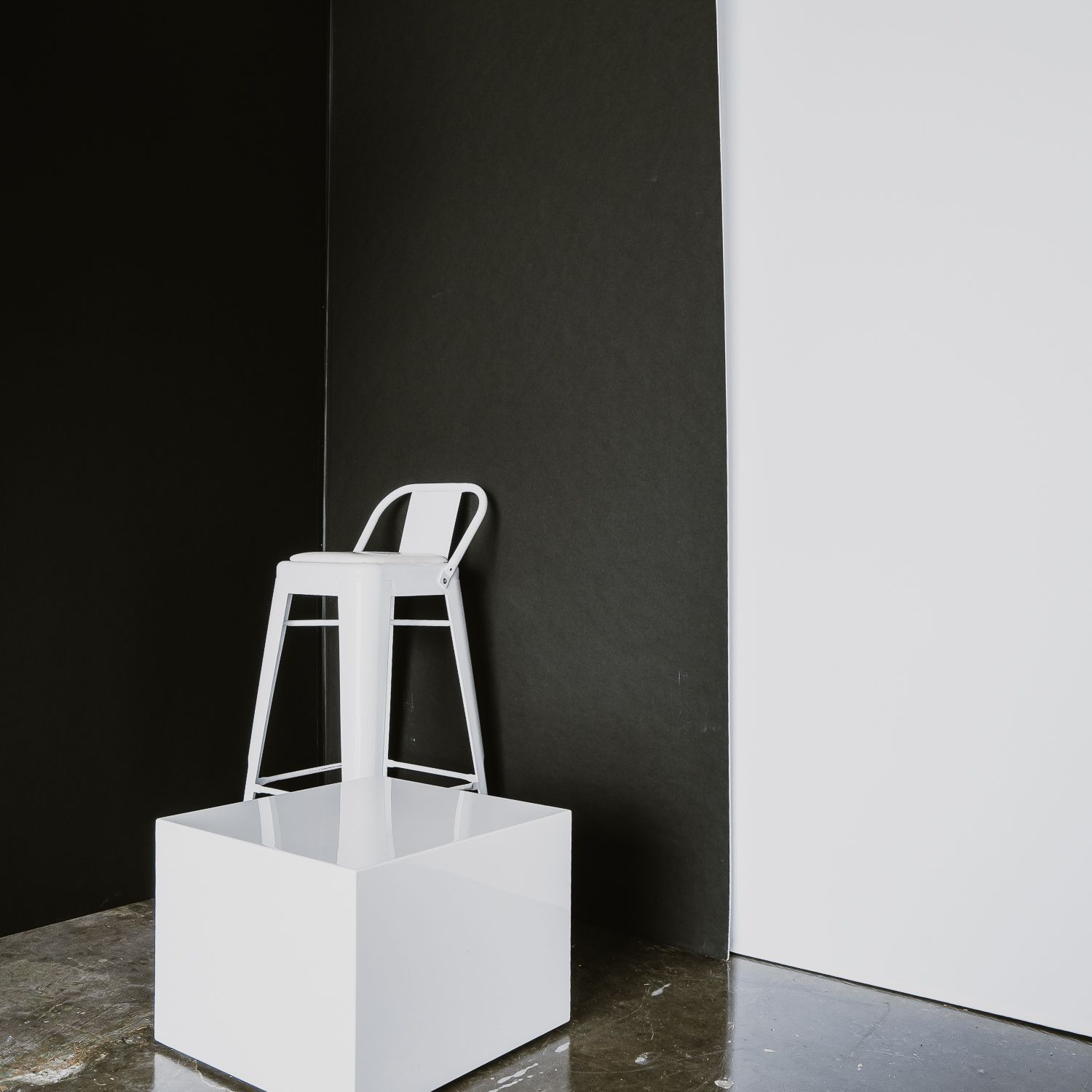 White chair and geometric shapes cast dramatic shadows against dark walls in a minimalist architectural study.