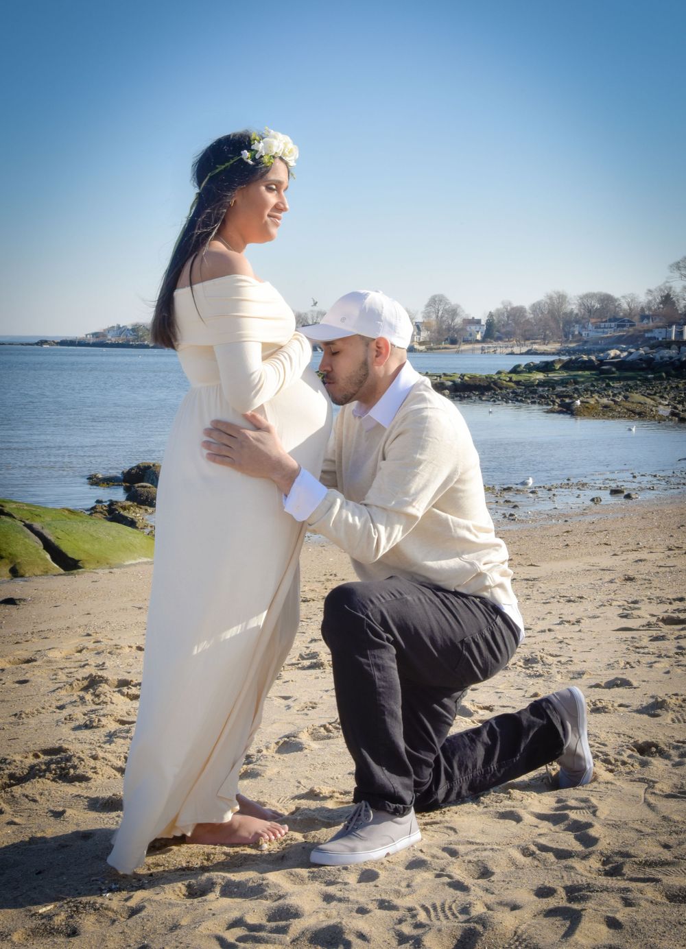 A romantic maternity photo shoot on a beach with an expectant couple posed by the waterfront on a sunny day.