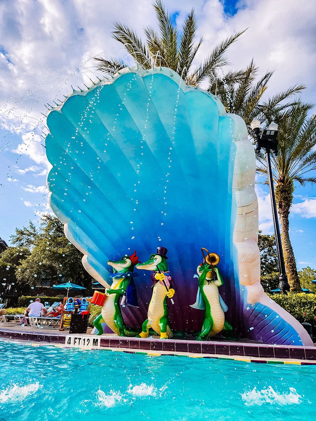 Sequence showing colorful turtle-shaped fountains spraying water in a resort pool surrounded by palm trees.