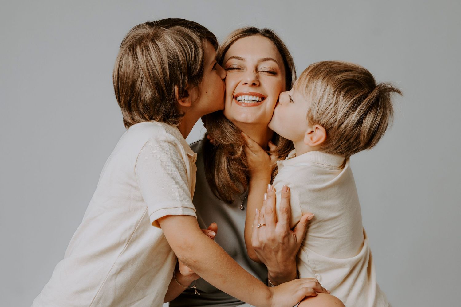 Mother and two young boys sharing a sweet moment of affection and laughter in a bright studio setting.