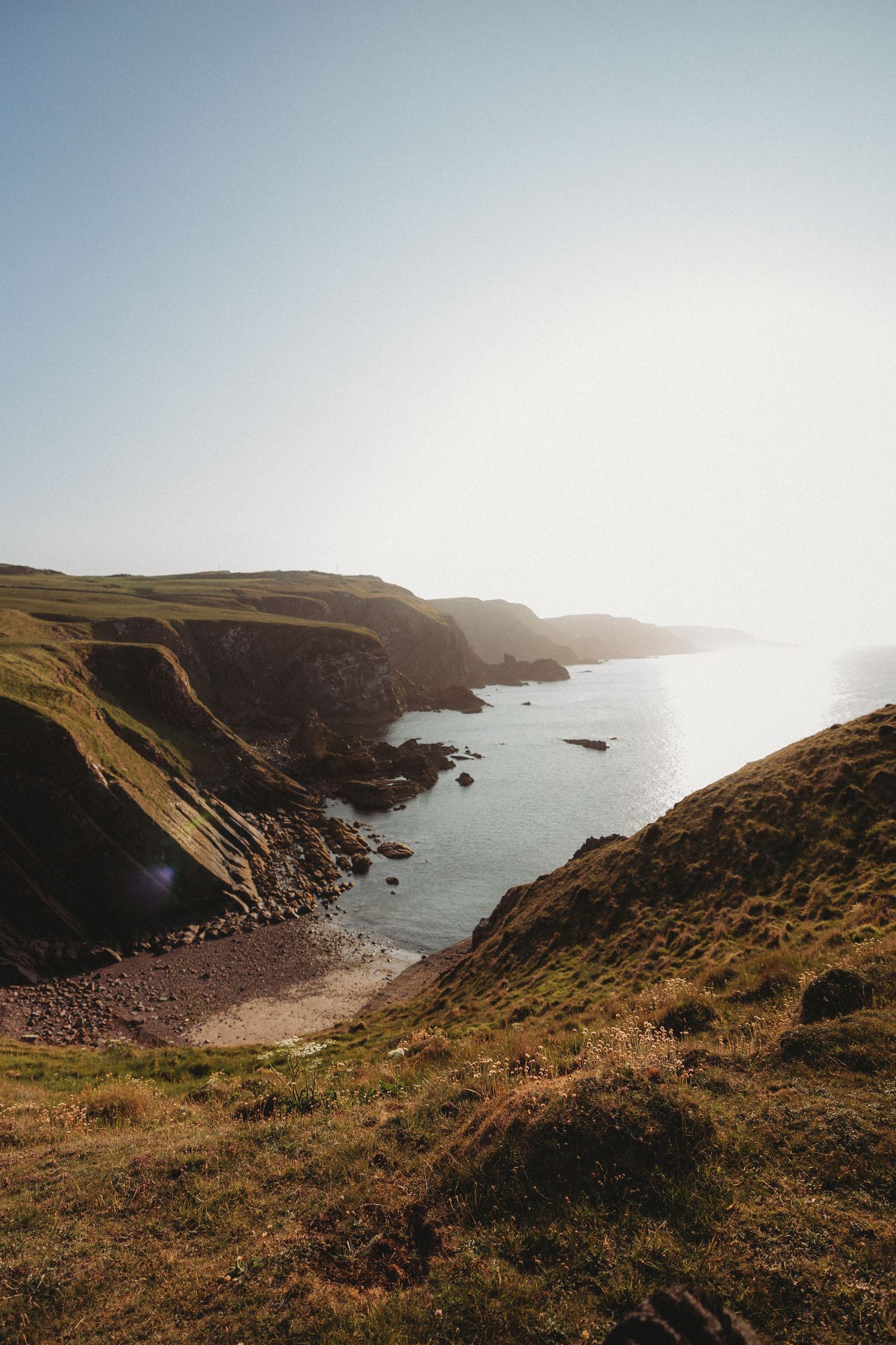 Winding coastal path along dramatic seaside cliffs under golden sunset light in Cornwall, England.