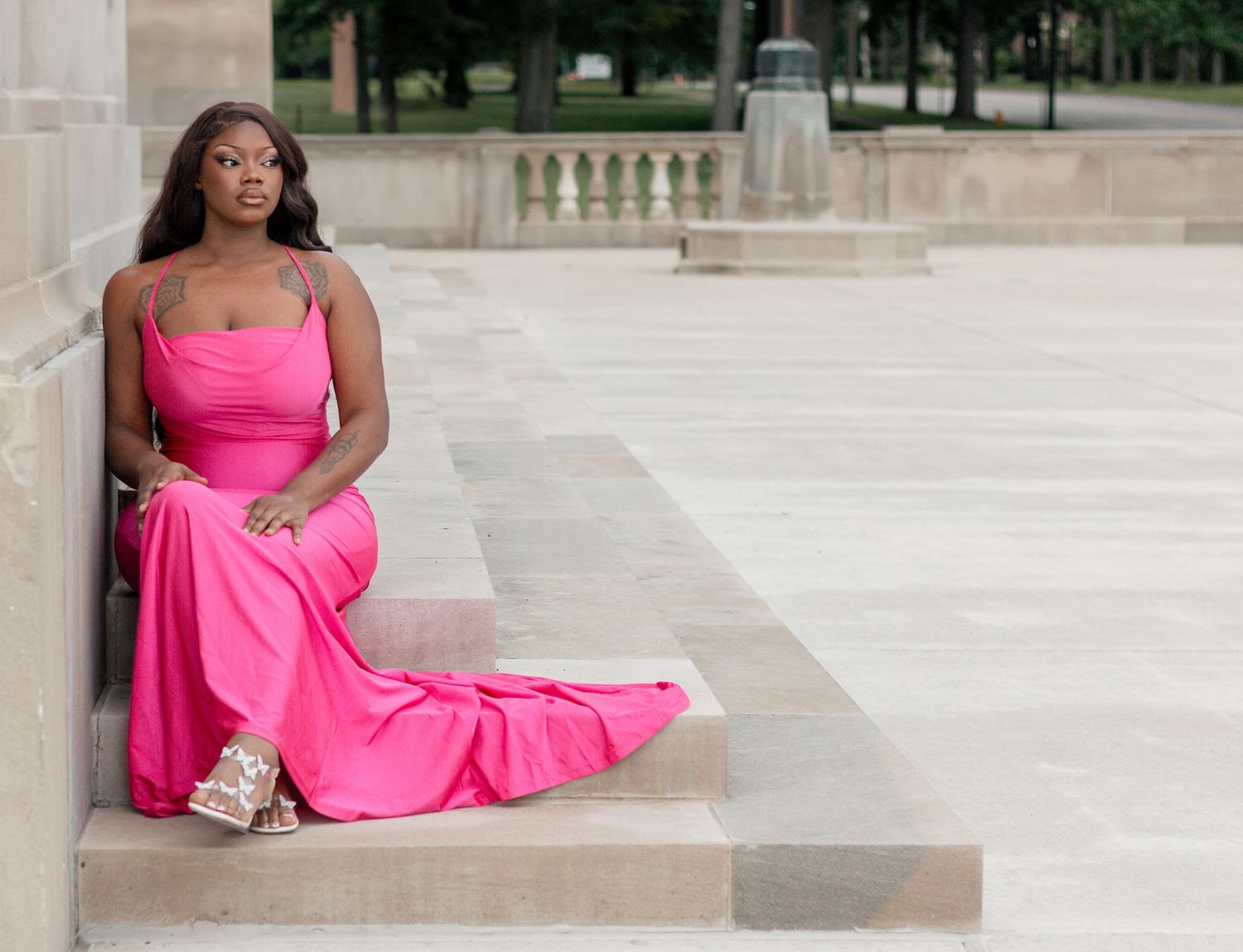 A person in a vibrant pink dress sits elegantly on stone steps with ornate stone balustrades in the background. stambaugh auditorium ohio