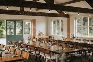 Rustic restaurant interior with exposed beams, white walls, green trim windows and wooden dining tables set for service.