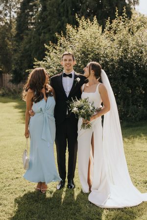 Wedding party stands together on sunny lawn with bride in white gown and bridesmaids in light blue dresses.