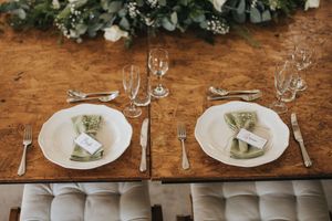 A rustic wedding reception table setting with blue napkins and gold silverware on a wooden table.