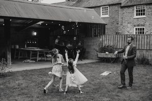 A black and white vintage photo shows children dancing in a backyard while an adult watches near a brick building.