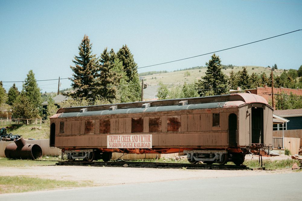 A collection of old railroad cars and buildings sit in a line at a vintage train station during daytime.
