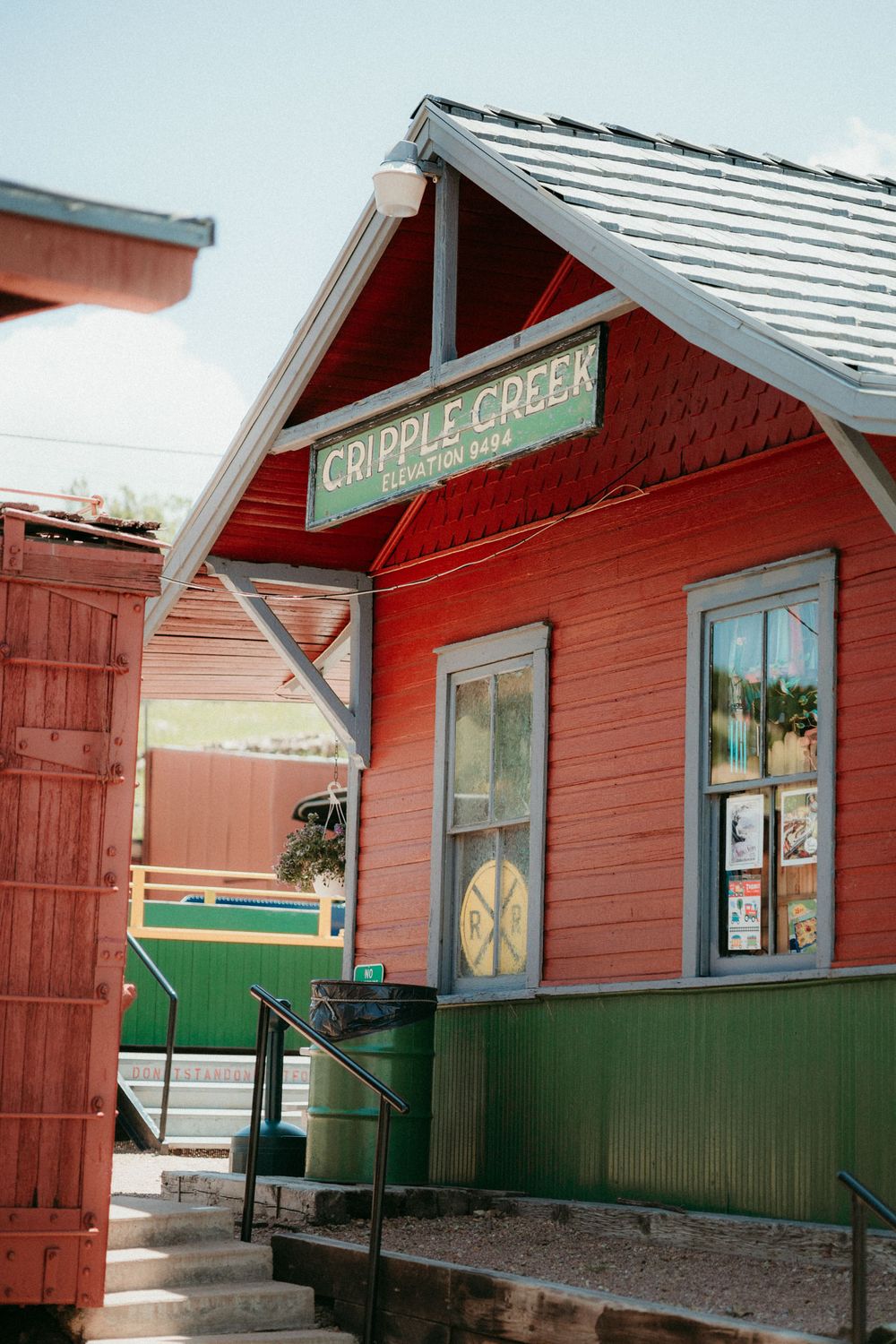Red and green painted historic Cripple Creek train station building with white trim and angled roof in Colorado.