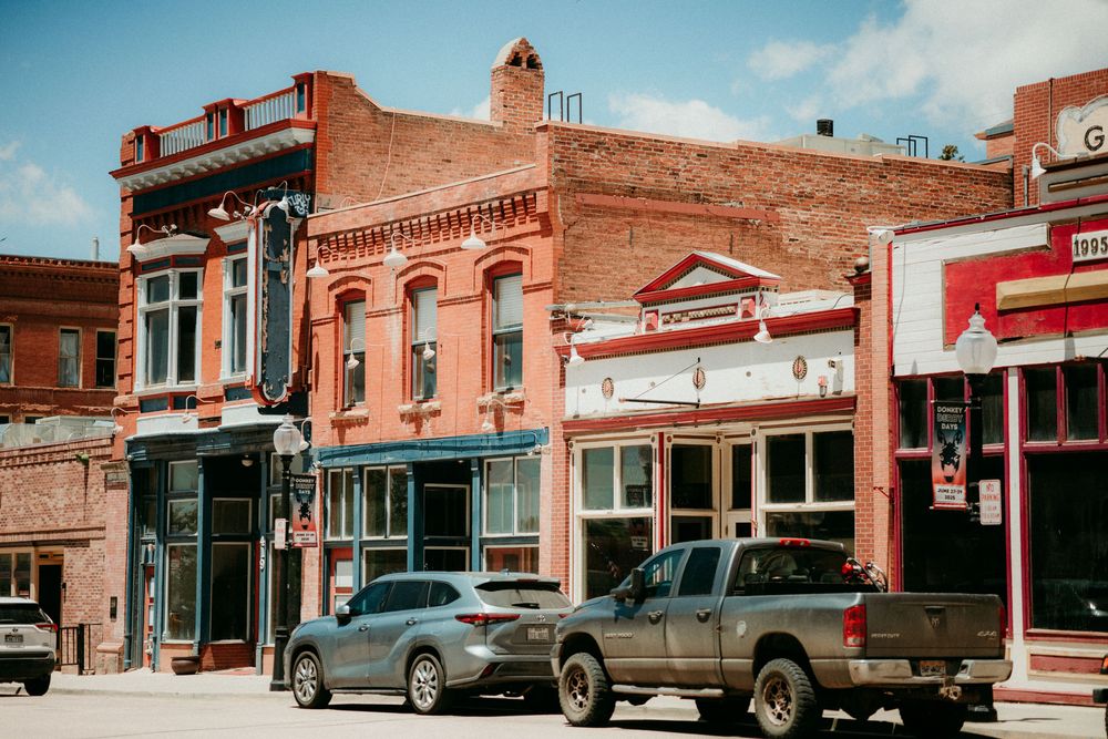 Vintage brick storefronts and pickup trucks line a historic small town main street with rustic charm.