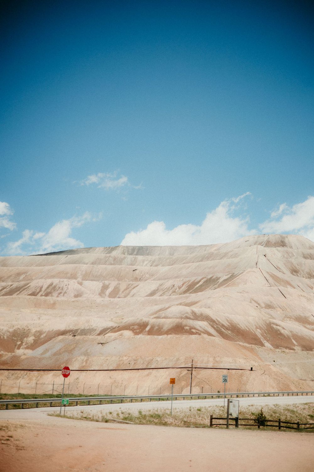 A panoramic view of barren desert hills in the backdrop with a long green fence stretching across the landscape.