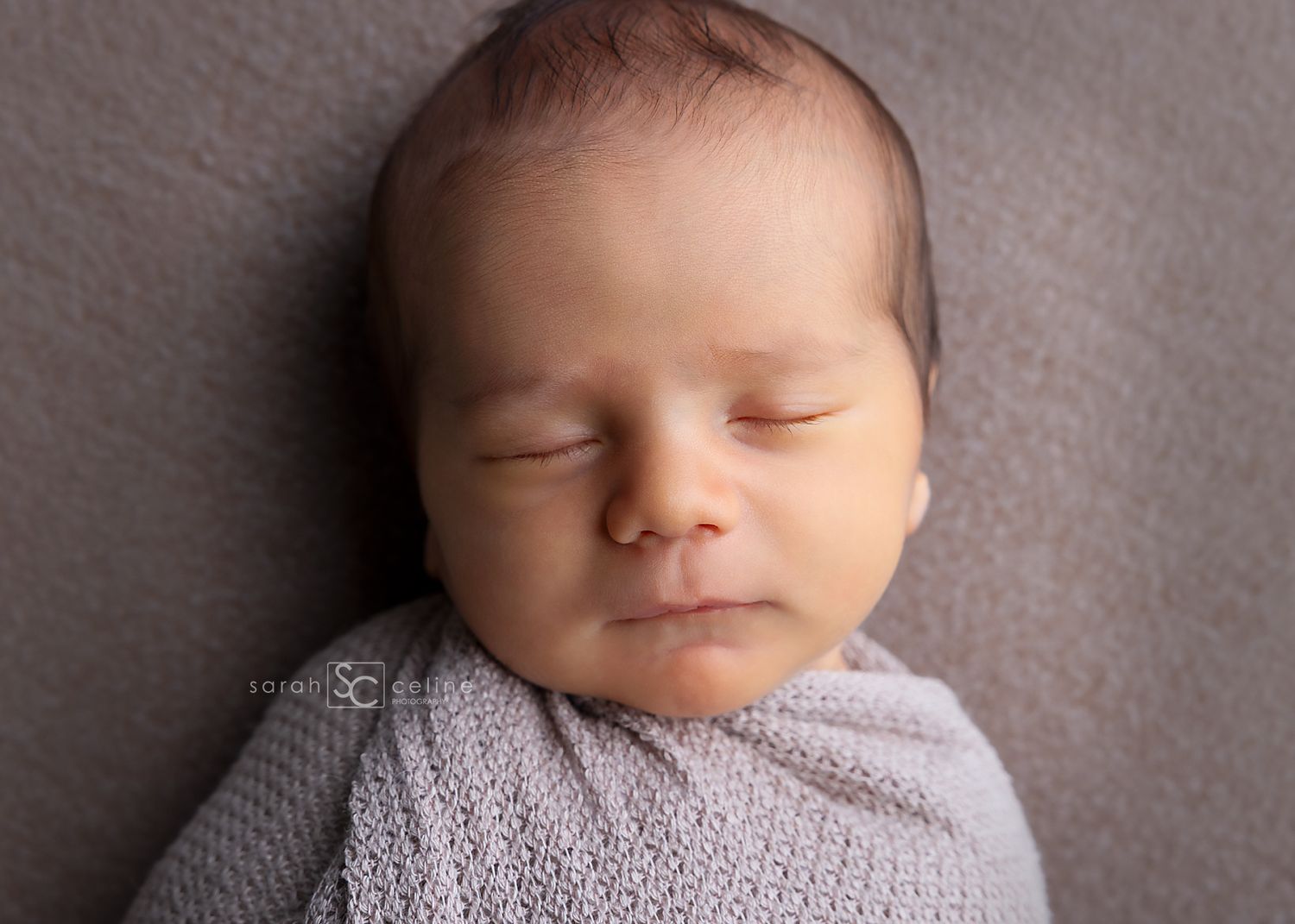 Peaceful sleeping newborn baby wrapped in soft gray knitted blanket on textured background.