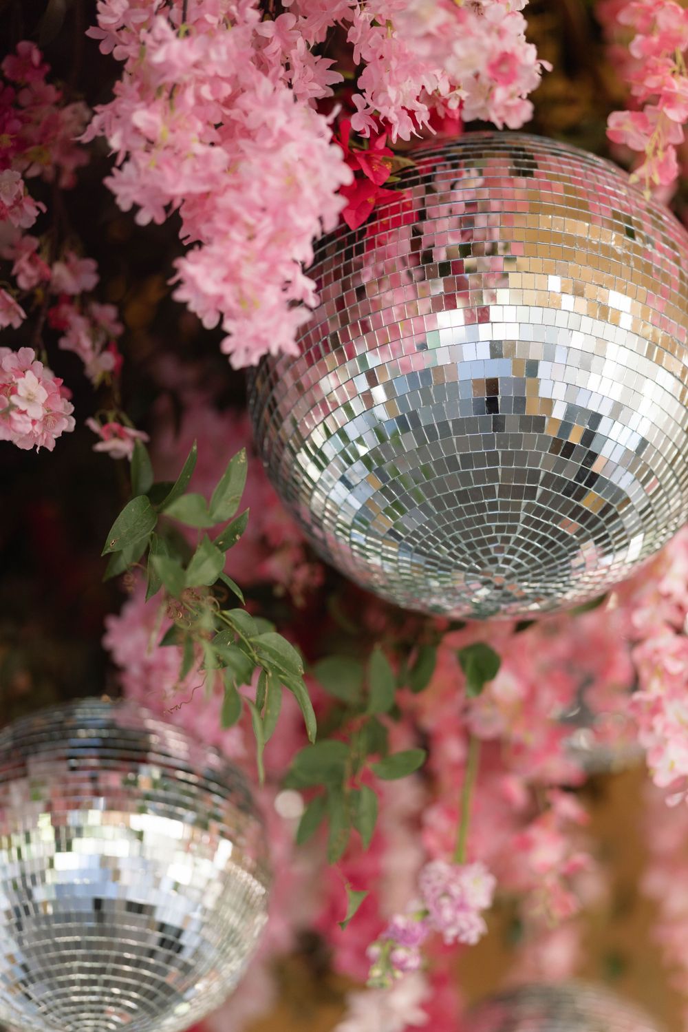 Shimmering disco balls hang elegantly among pink cherry blossoms creating a dreamy party atmosphere.