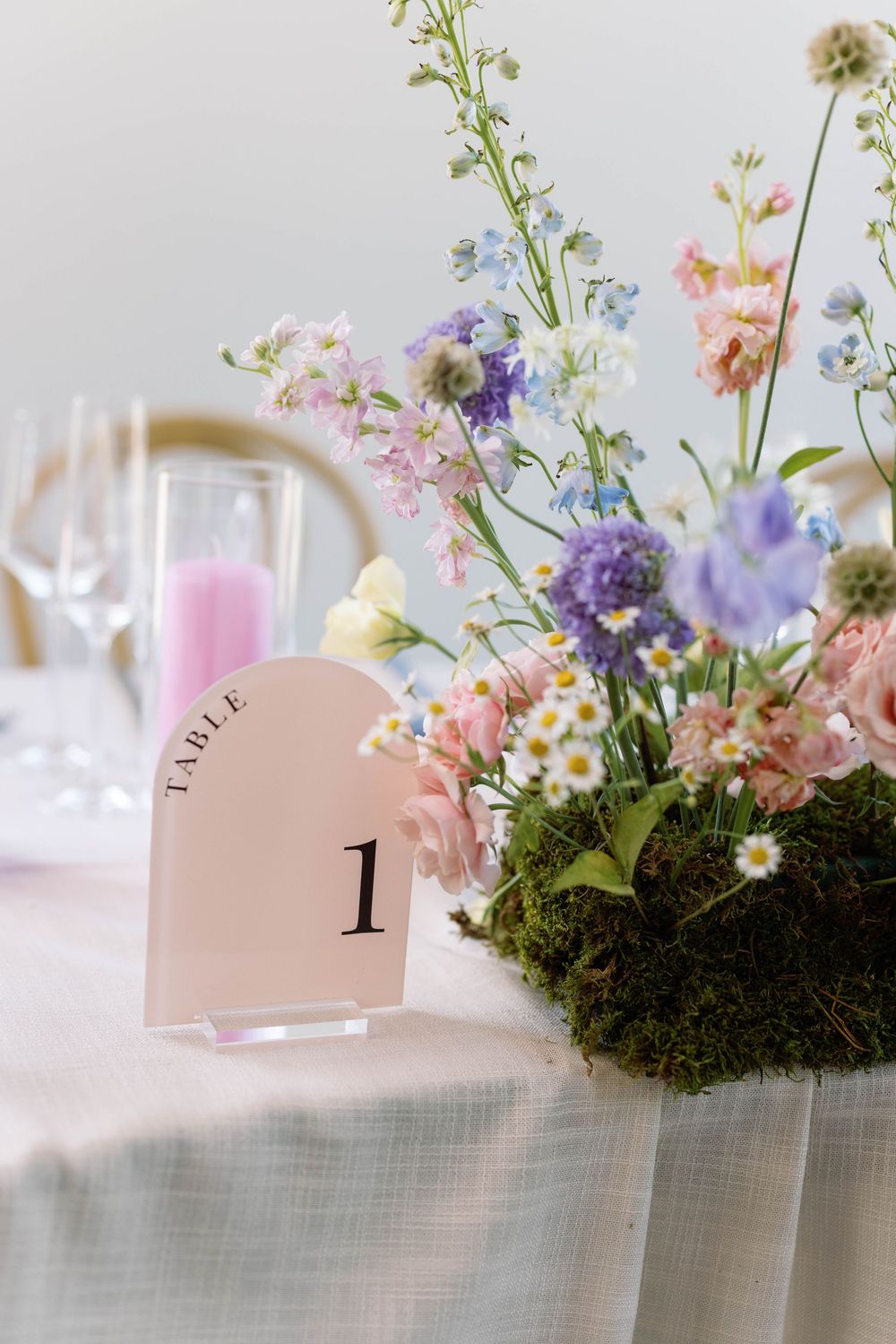 Elegant wedding table centerpieces featuring delicate wildflowers, moss, and table numbers in soft pastel colors.