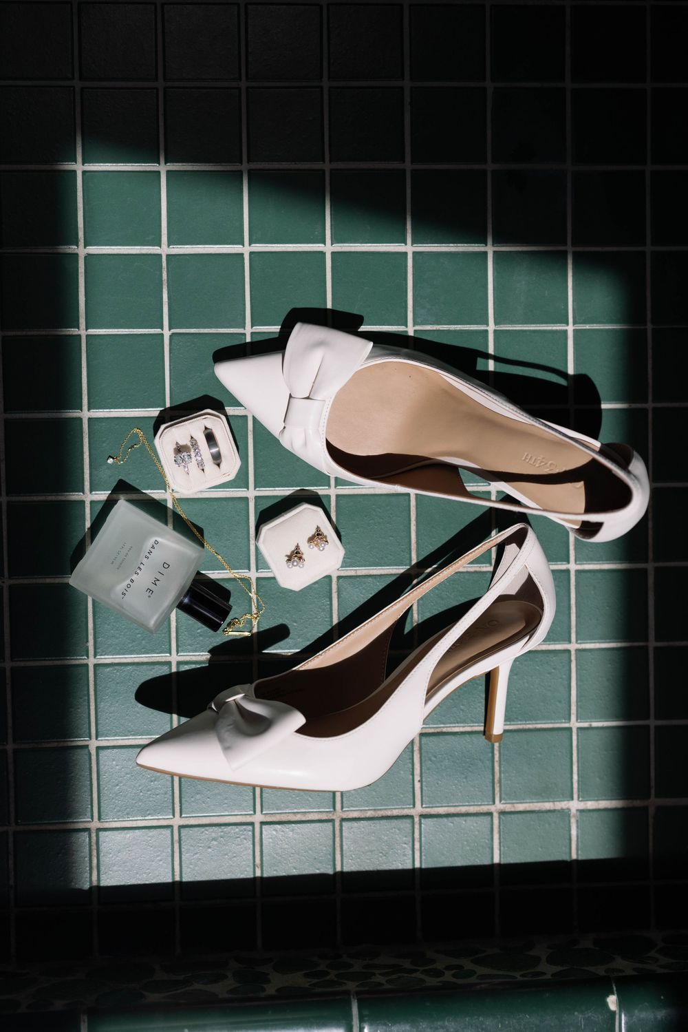Elegant white leather stiletto heels artistically photographed against dark green tiled wall.