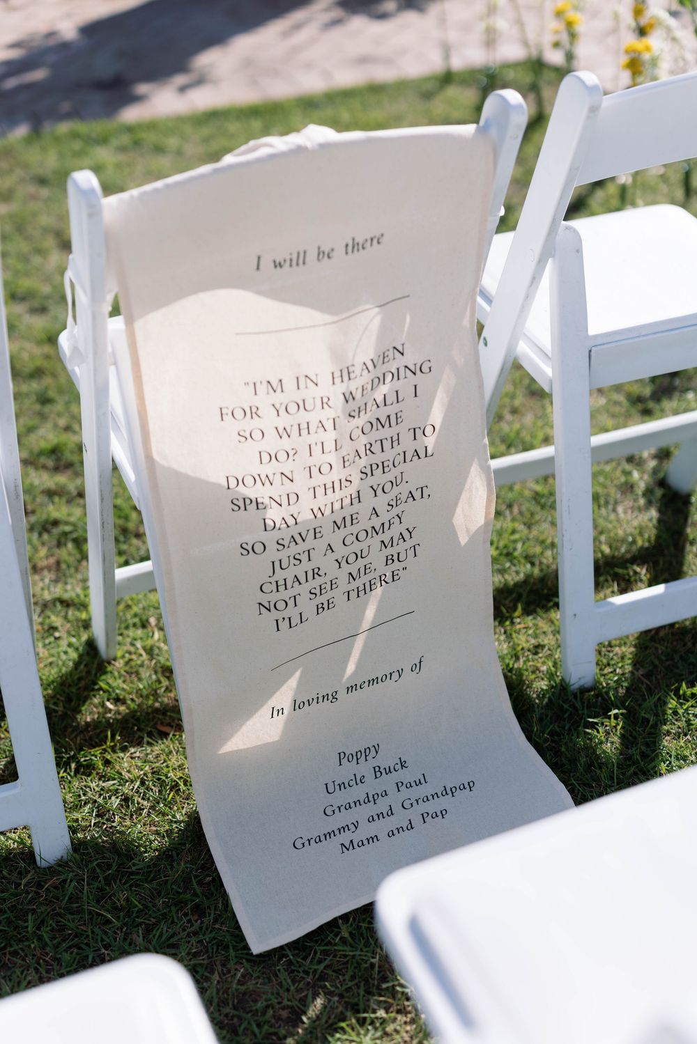White ceremony chairs display heartfelt memorial messages printed on paper during an outdoor wedding setup.