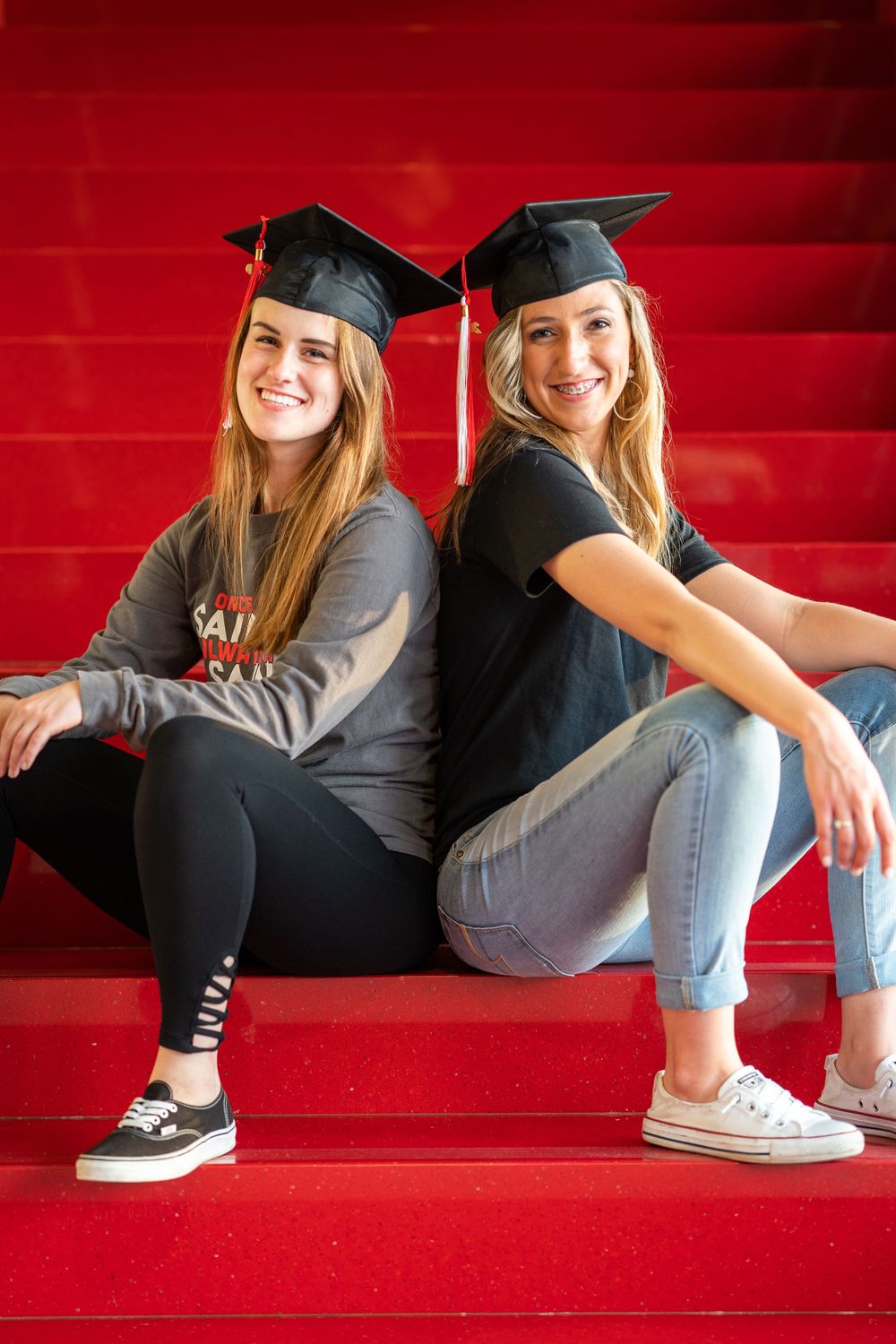 Graduation portrait of two college graduates in caps sitting on red stairs.