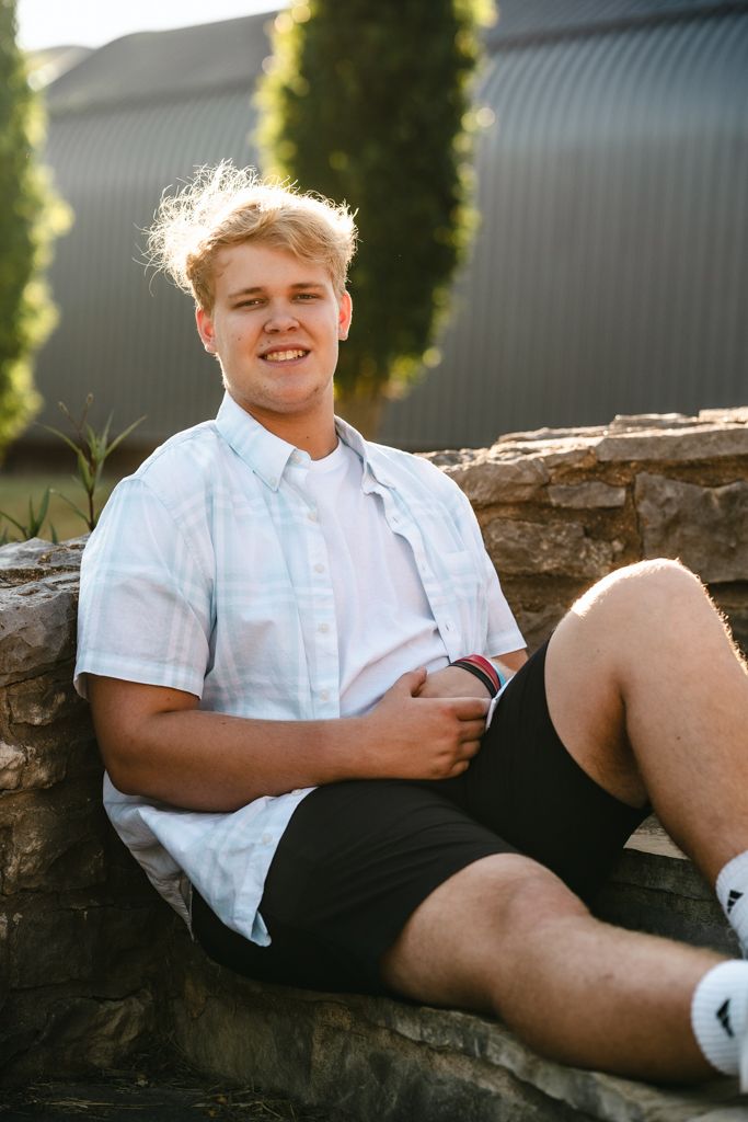 Senior portrait of high school student sitting in front of a rock wall.