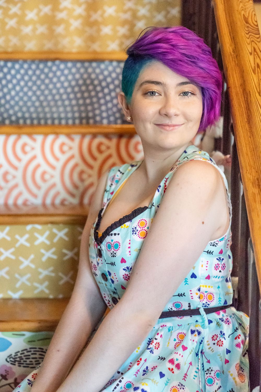 Senior portrait of high school purple haired girl wearing a blue dress sitting on fun colored stairs.
