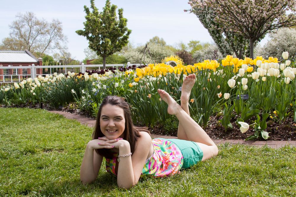 Senior portrait of high school girl wearing colorful clothes in front of tulips at a garden. Laying down with her chin on her hands.
